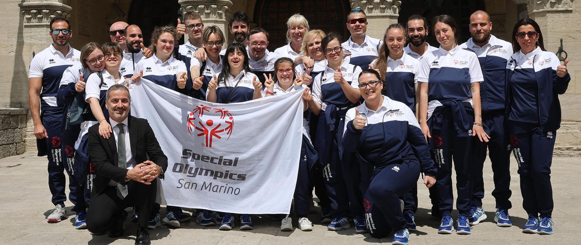 Gruppo di atleti Special Olympics San Marino sorridenti con bandiera.